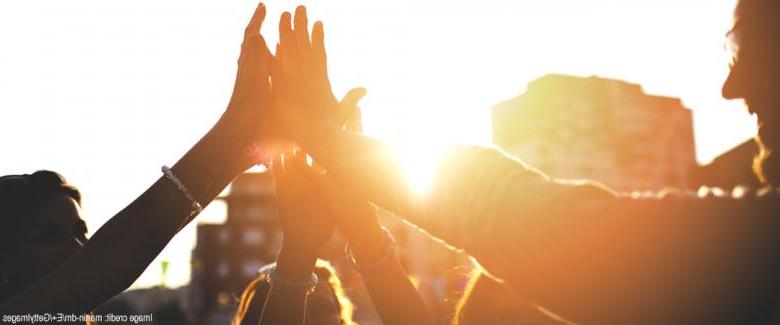 siluetas de un grupo de personas chocando las manos al atardecer con efecto de resplandor solar