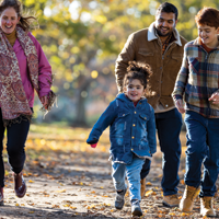 一位拉美裔父亲和一位白人母亲带着女儿和儿子在秋天的公园里散步的照片